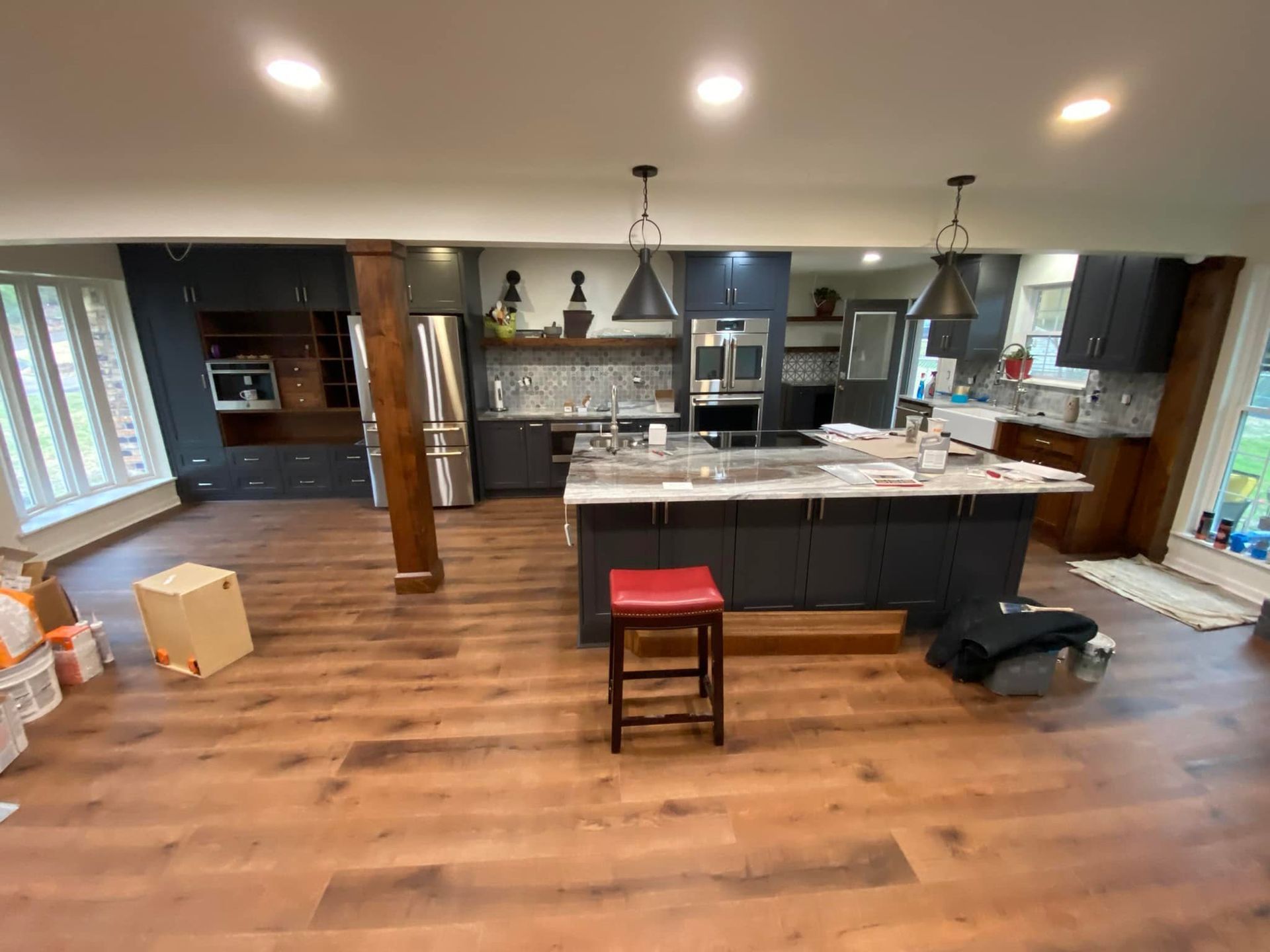 Spacious kitchen with dark gray cabinets, island, stainless steel appliances, and wood-look flooring. A red stool sits at the island.