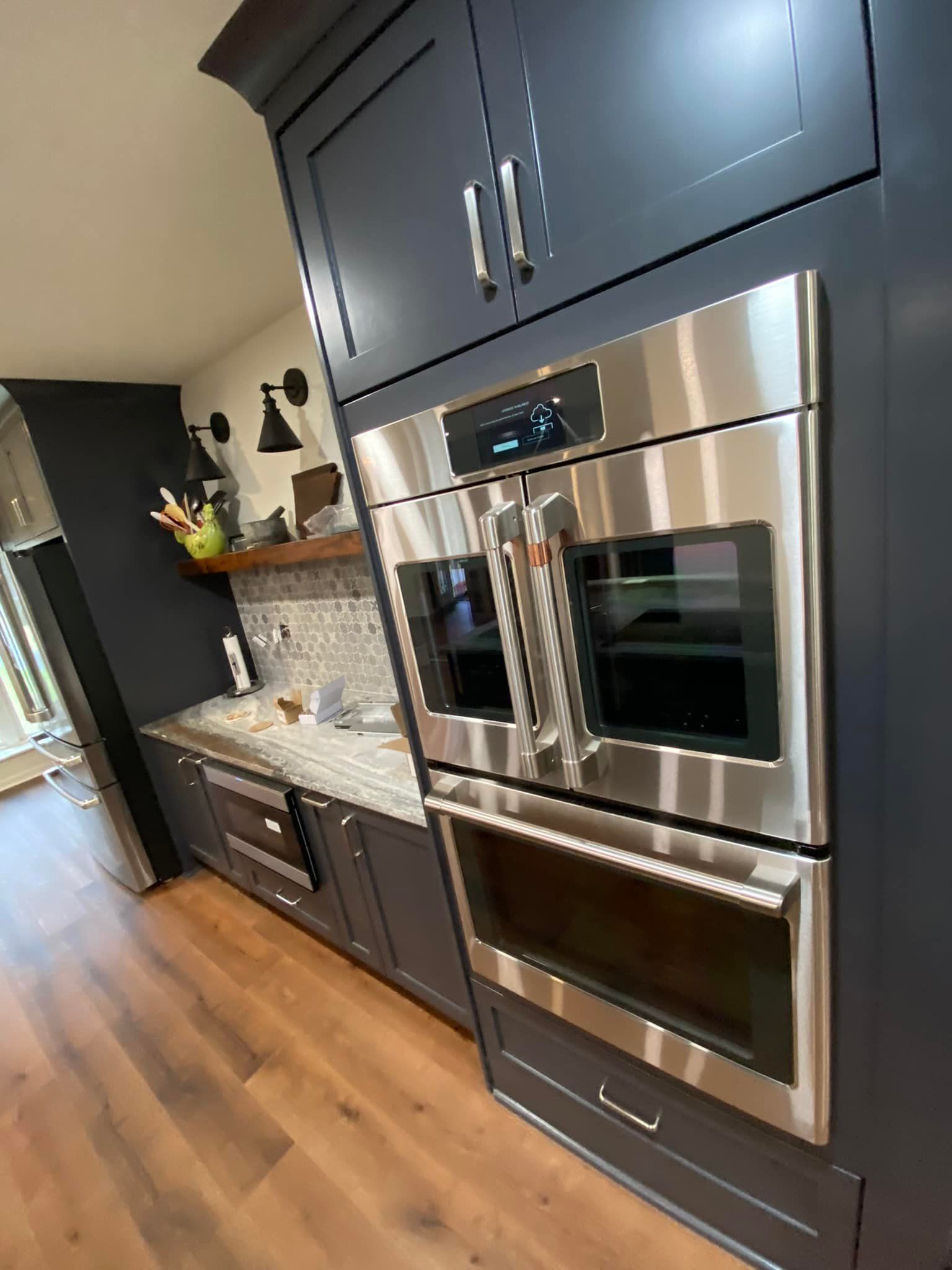 Built-in stainless steel double oven in a navy blue kitchen cabinet. Wooden floor and a small countertop.