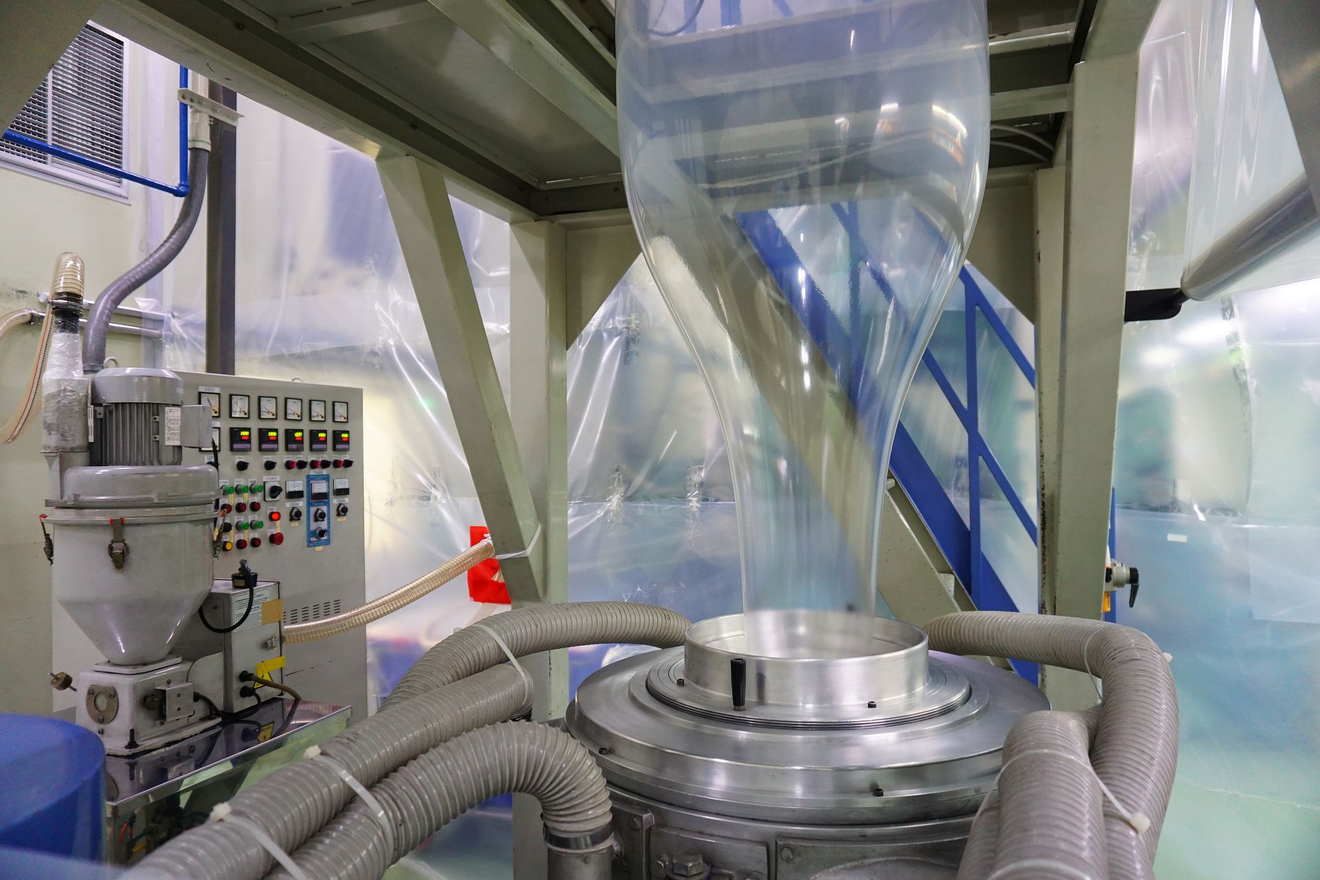 Plastic bag manufacturing machine in a factory. Transparent plastic tube rising from silver machinery.