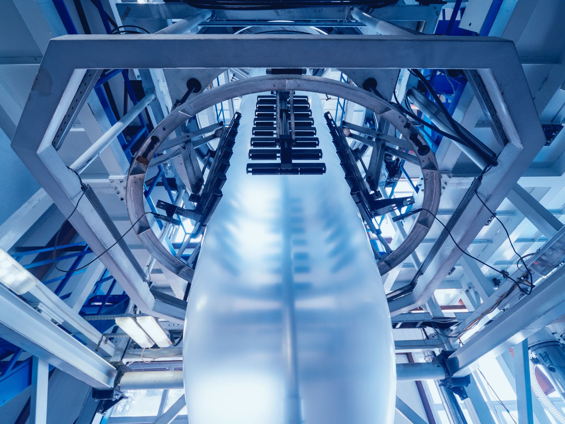 Plastic film extrusion machine, producing a translucent plastic sheet. Industrial setting, blue tones.