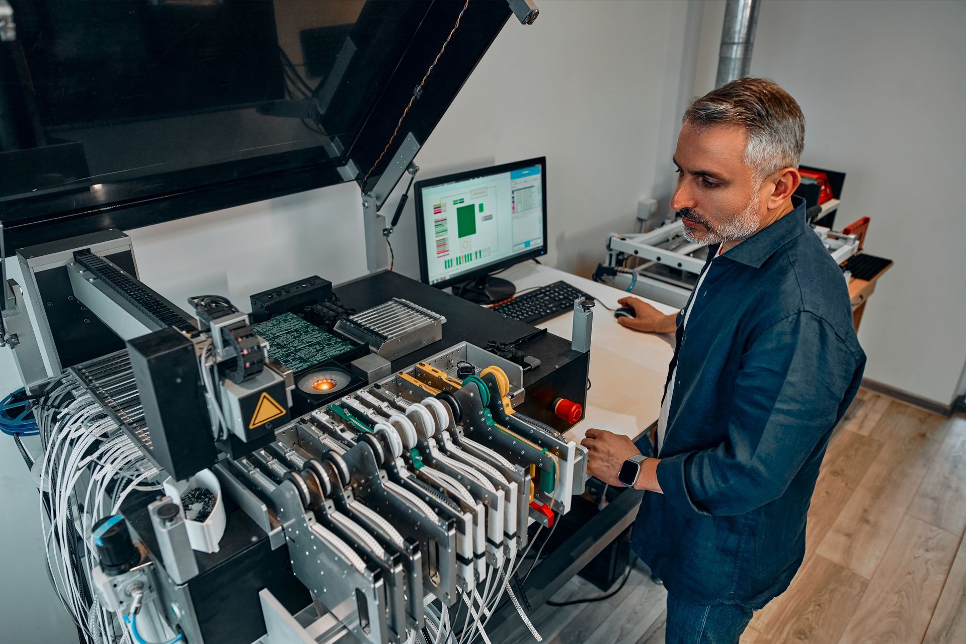 Man operating circuit board assembly machine with computer in a lab.