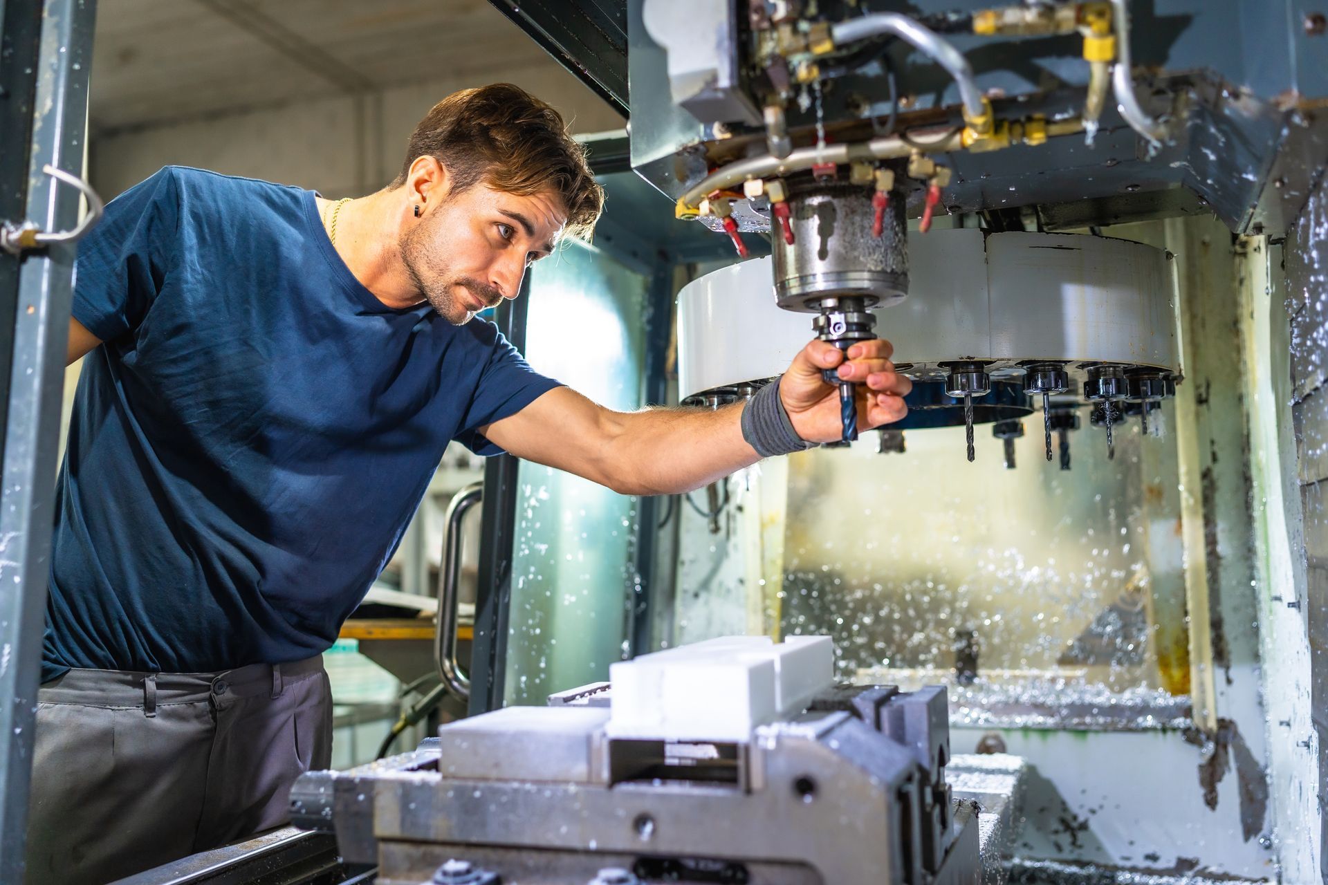 Man working on a CNC machine, observing the cutting process with focused attention.