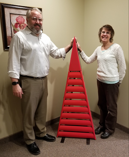 A man and woman standing next to a large red triangle-shaped object, high-fiving it.