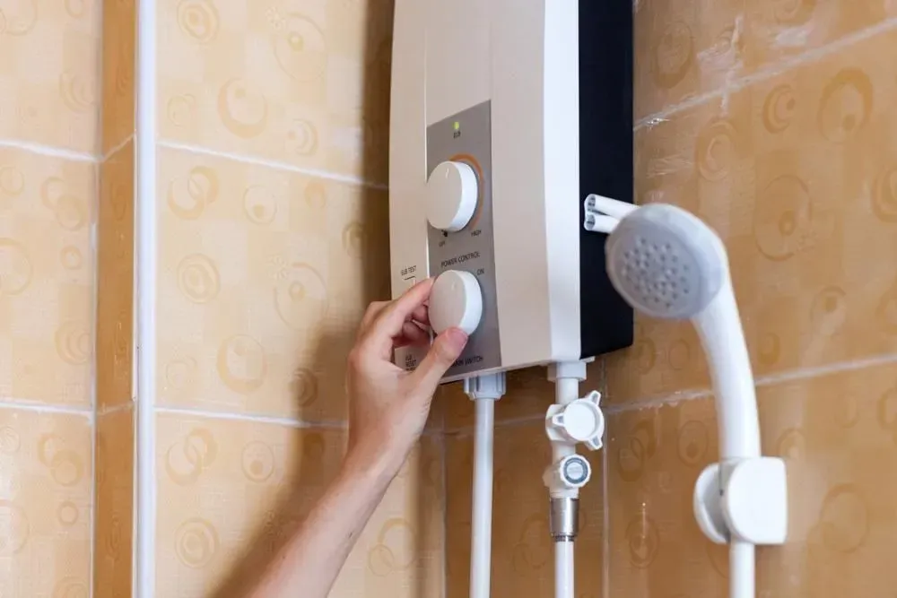 Hand adjusting the dial on a wall-mounted electric shower in a tiled bathroom