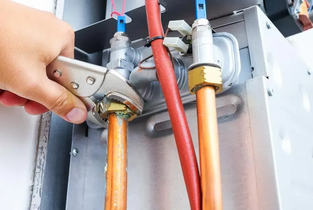 Hand adjusting a brass gas valve connected to copper pipes in a metal appliance cabinet