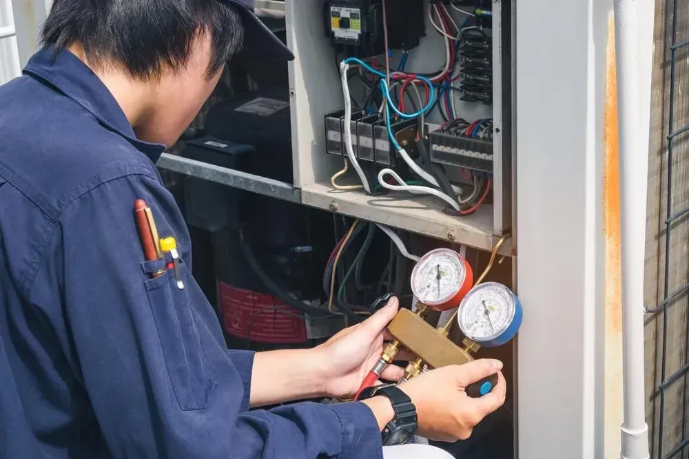 Technician inspecting HVAC unit with gauges and tools inside an open electrical cabinet