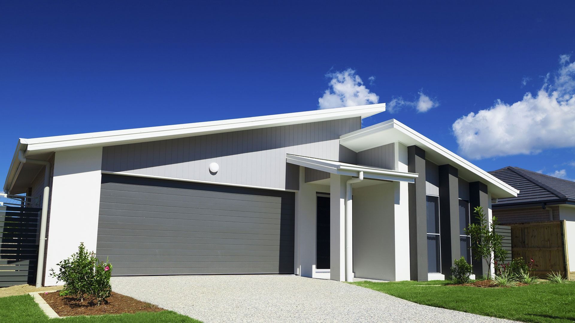 Modern white house with a gray garage door, front entry, and blue sky above