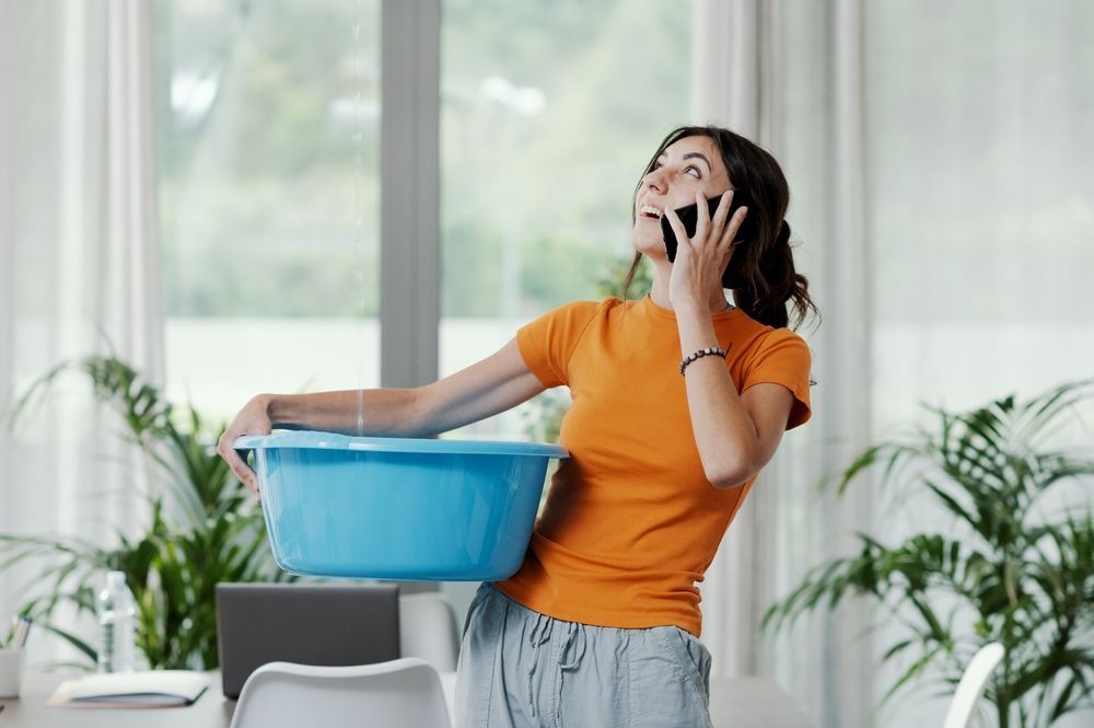 Woman in an orange shirt holding her nose beside a blue bucket in a bright room