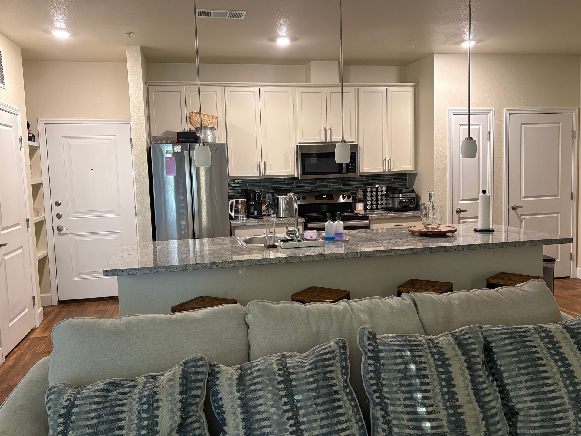 A kitchen with cream cabinets, stainless steel appliances, and an island with stools, seen from a couch.