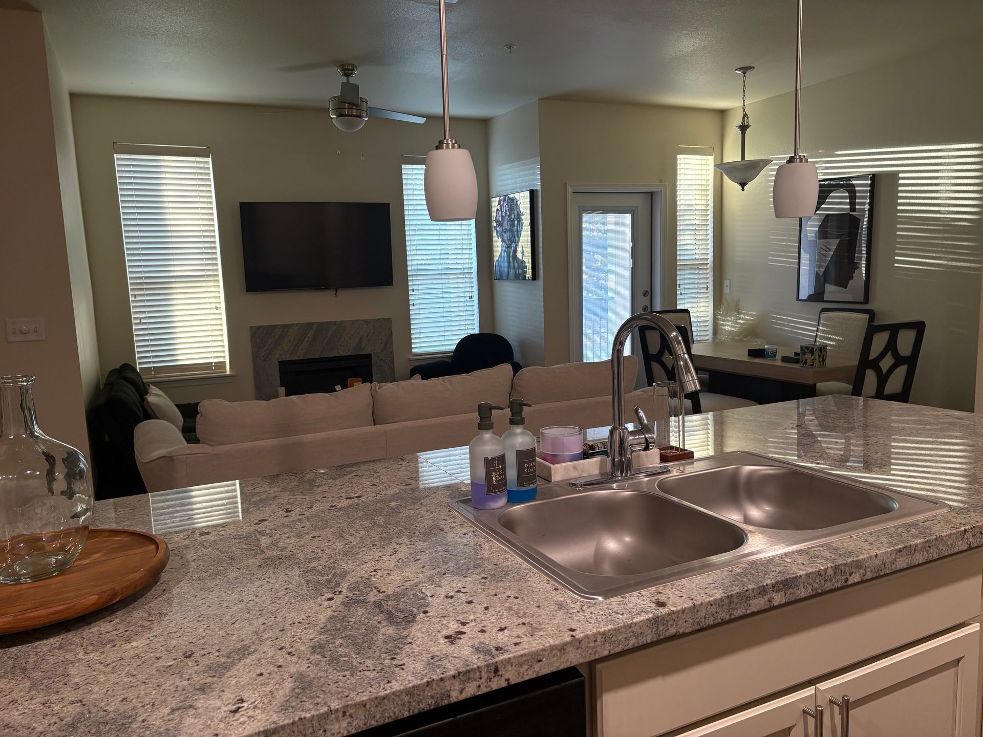 Kitchen with granite countertop and sink, looking into living room with a couch, fireplace, and TV.