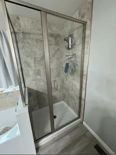 A shower stall with sliding glass doors and a gray tile interior. Silver frame.
