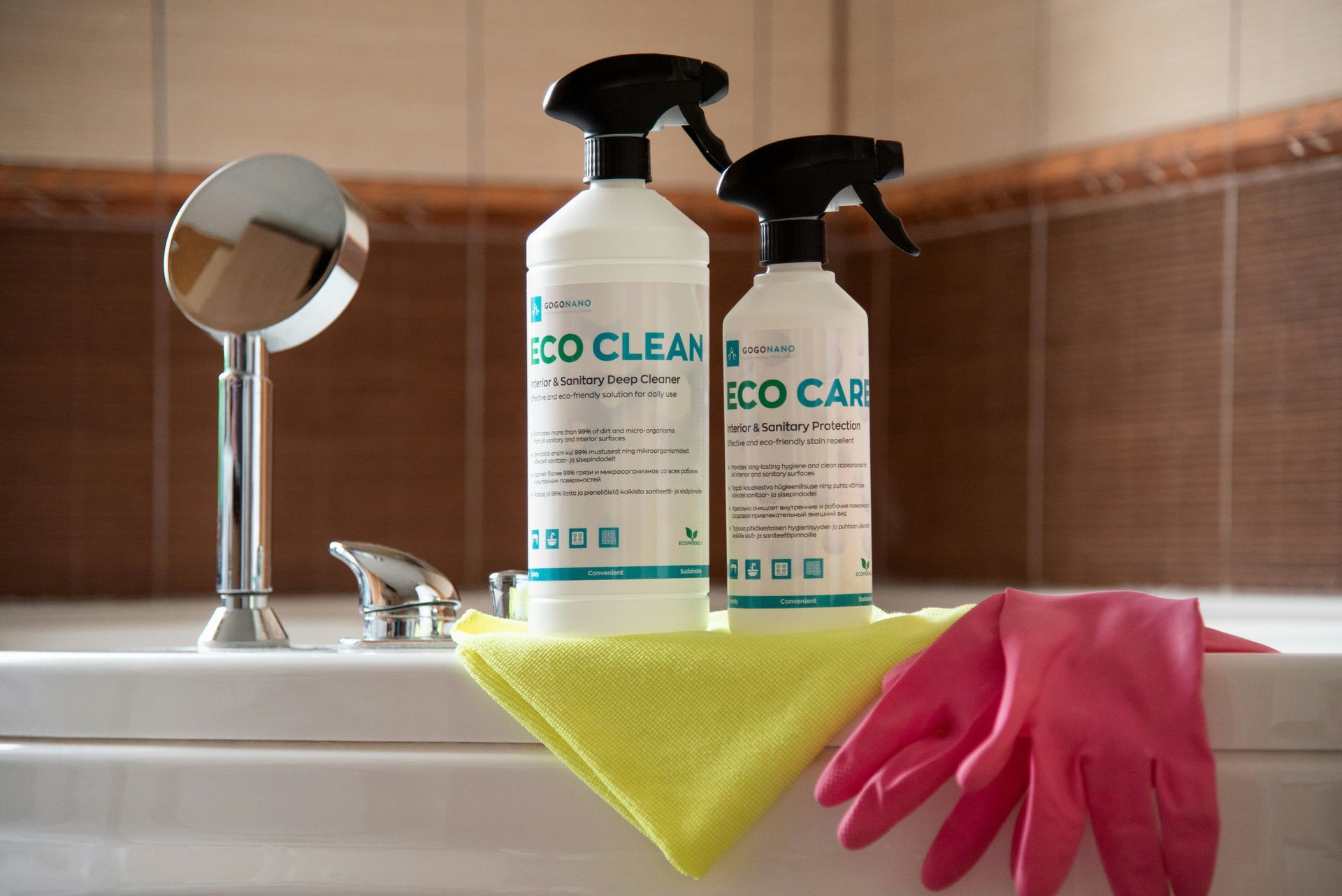 Two spray bottles , a towel , and pink gloves are sitting on a bathtub.