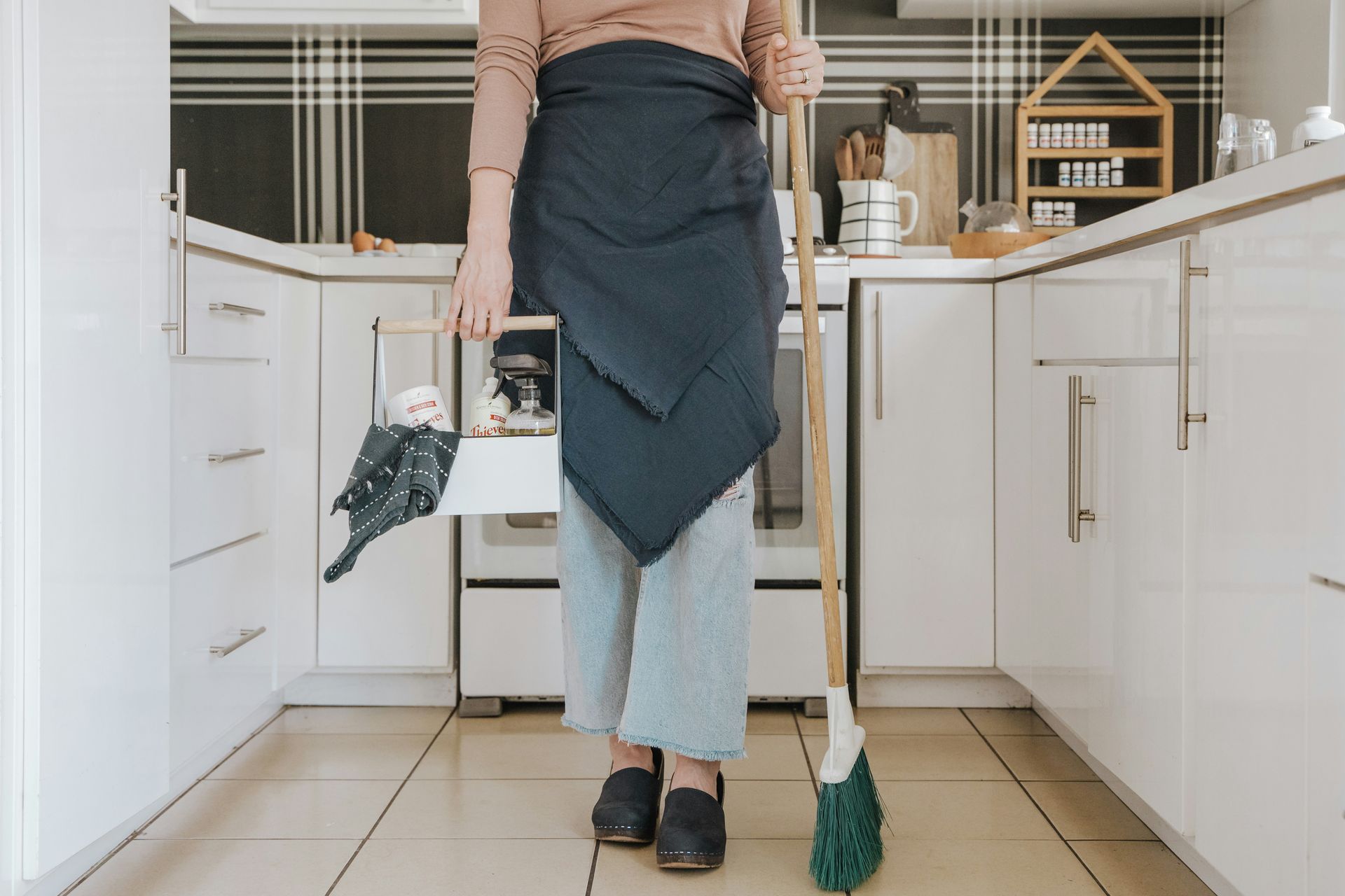 A woman is standing in a kitchen holding a mop and a basket.