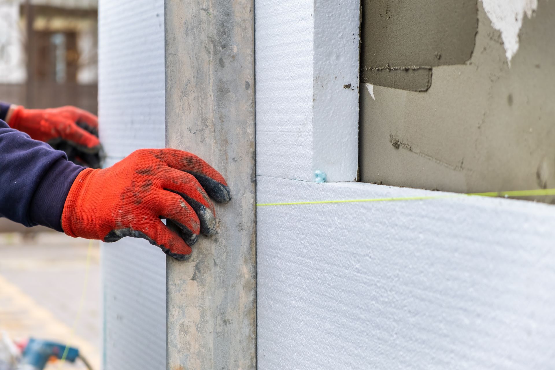 A man wearing red gloves is measuring a wall with a tape measure.