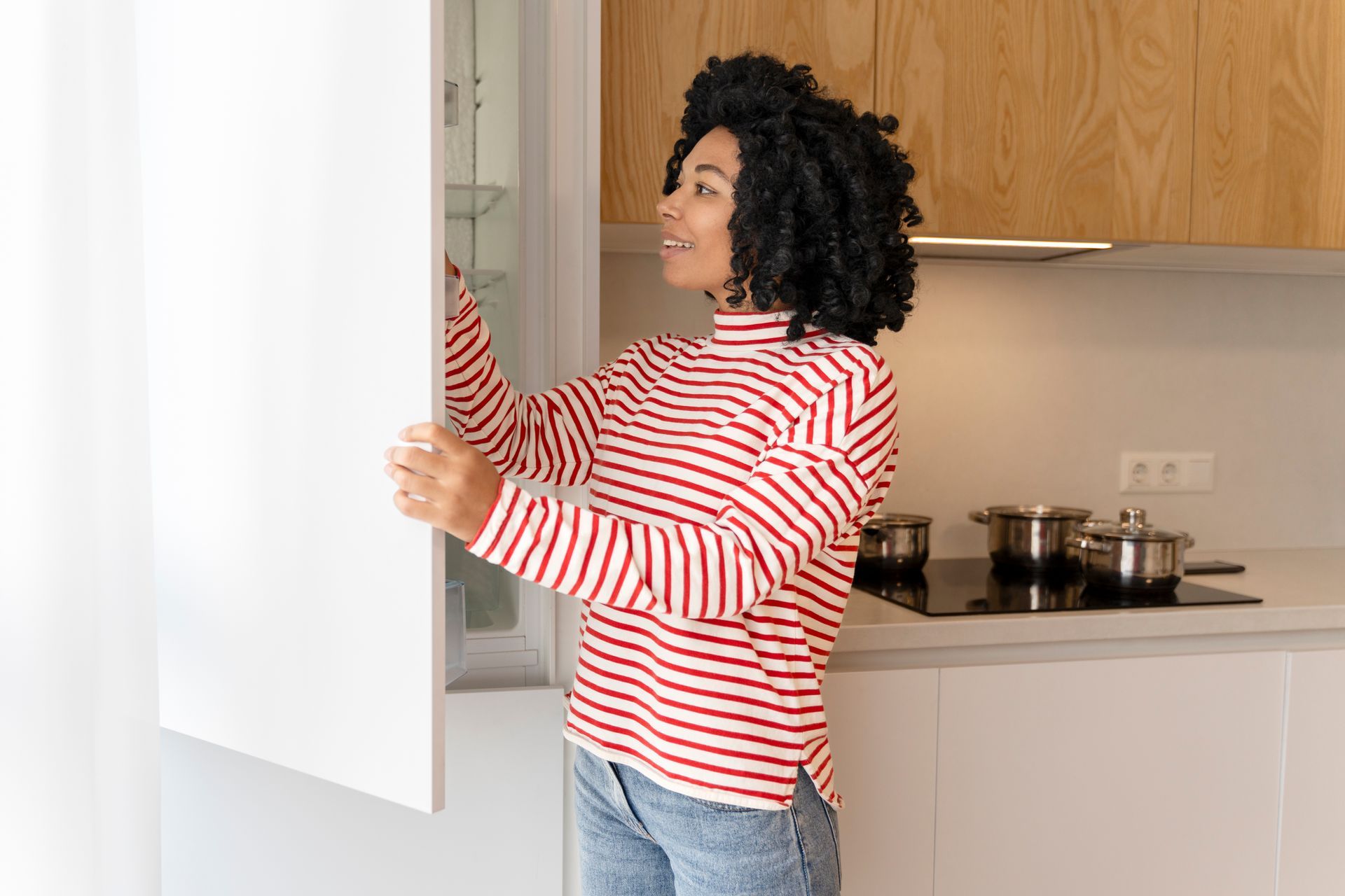 A woman is opening a refrigerator door in a kitchen.