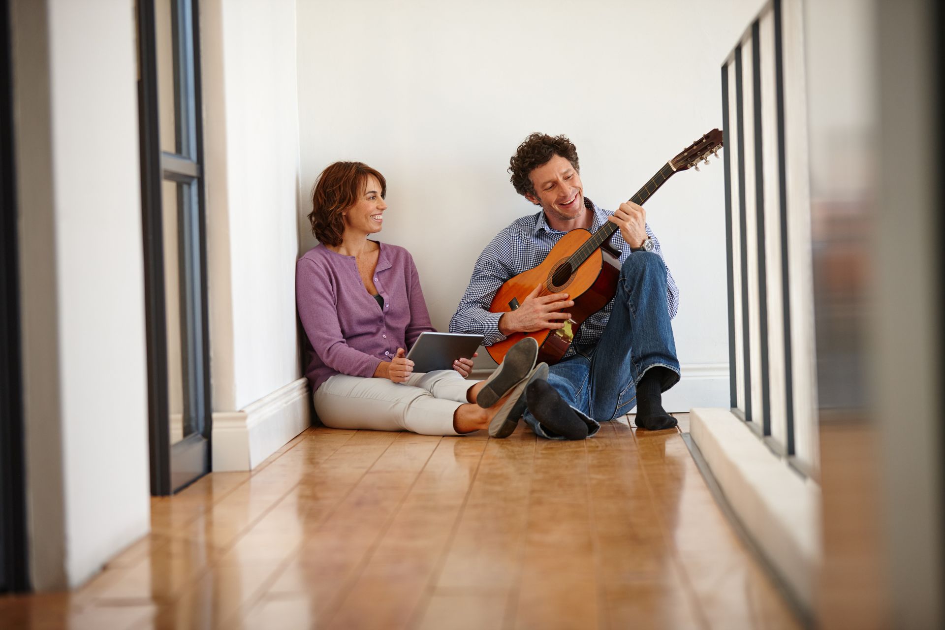 A man is playing a guitar to a woman while they sit on the floor.