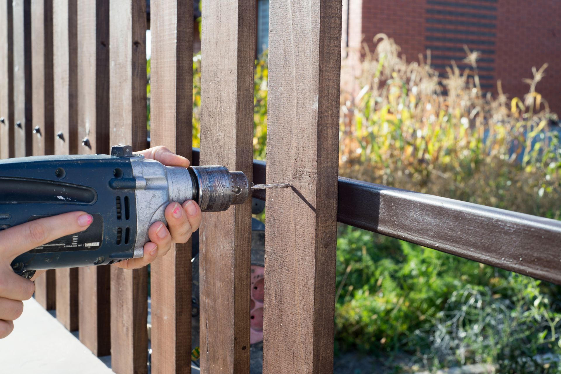 A person is using a drill to drill a hole in a wooden fence.