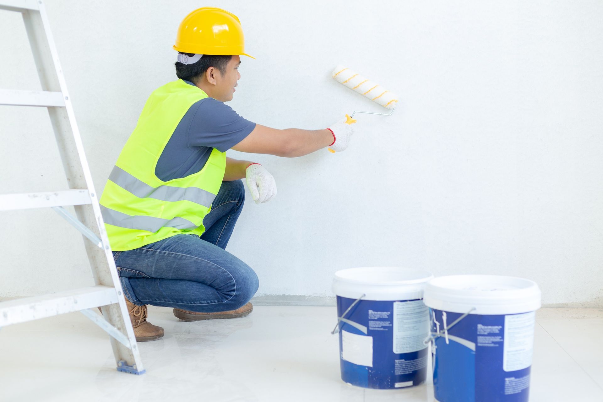 A man is kneeling down and painting a wall with a paint roller.
