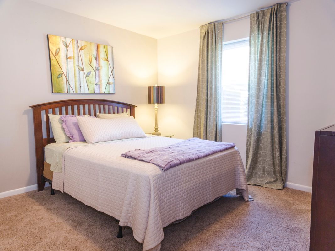 A bedroom with a bed , dresser , lamp and window.