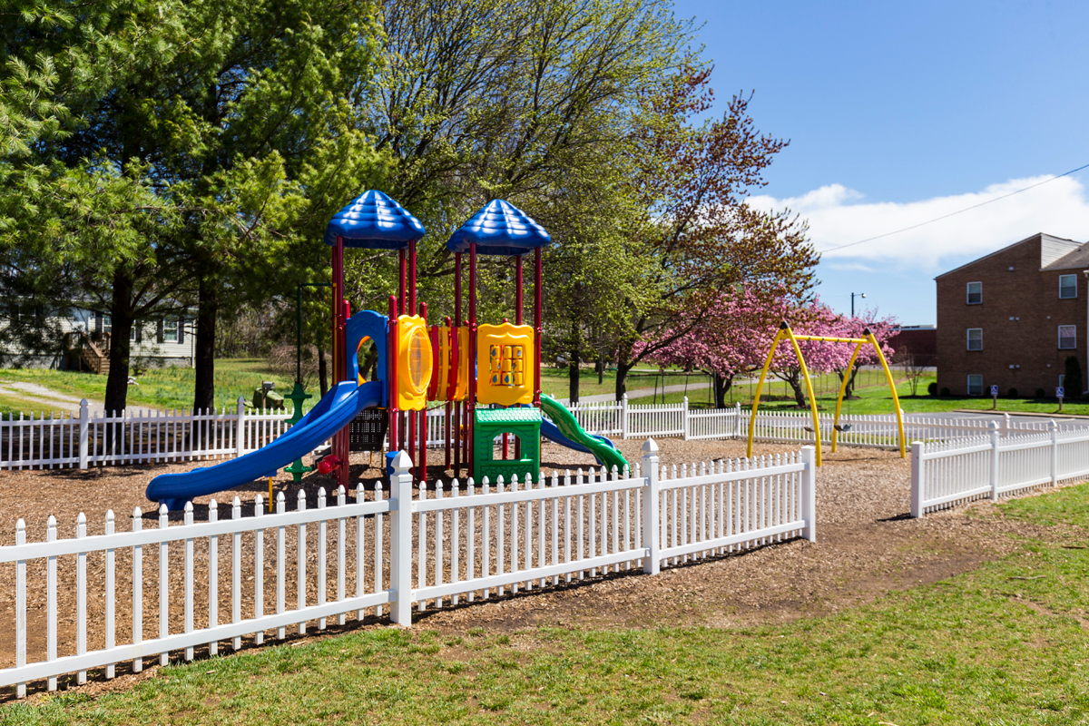 A colorful playground with a white picket fence in a park.