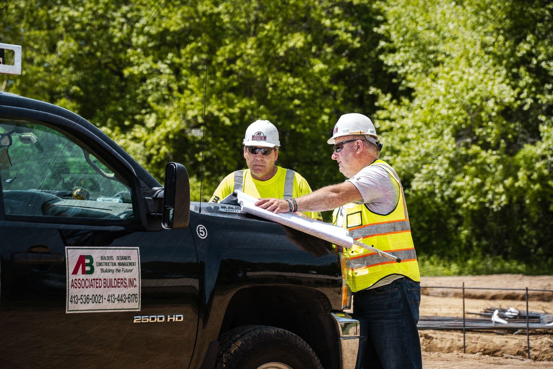 Two construction workers are standing next to a truck looking at a blueprint.