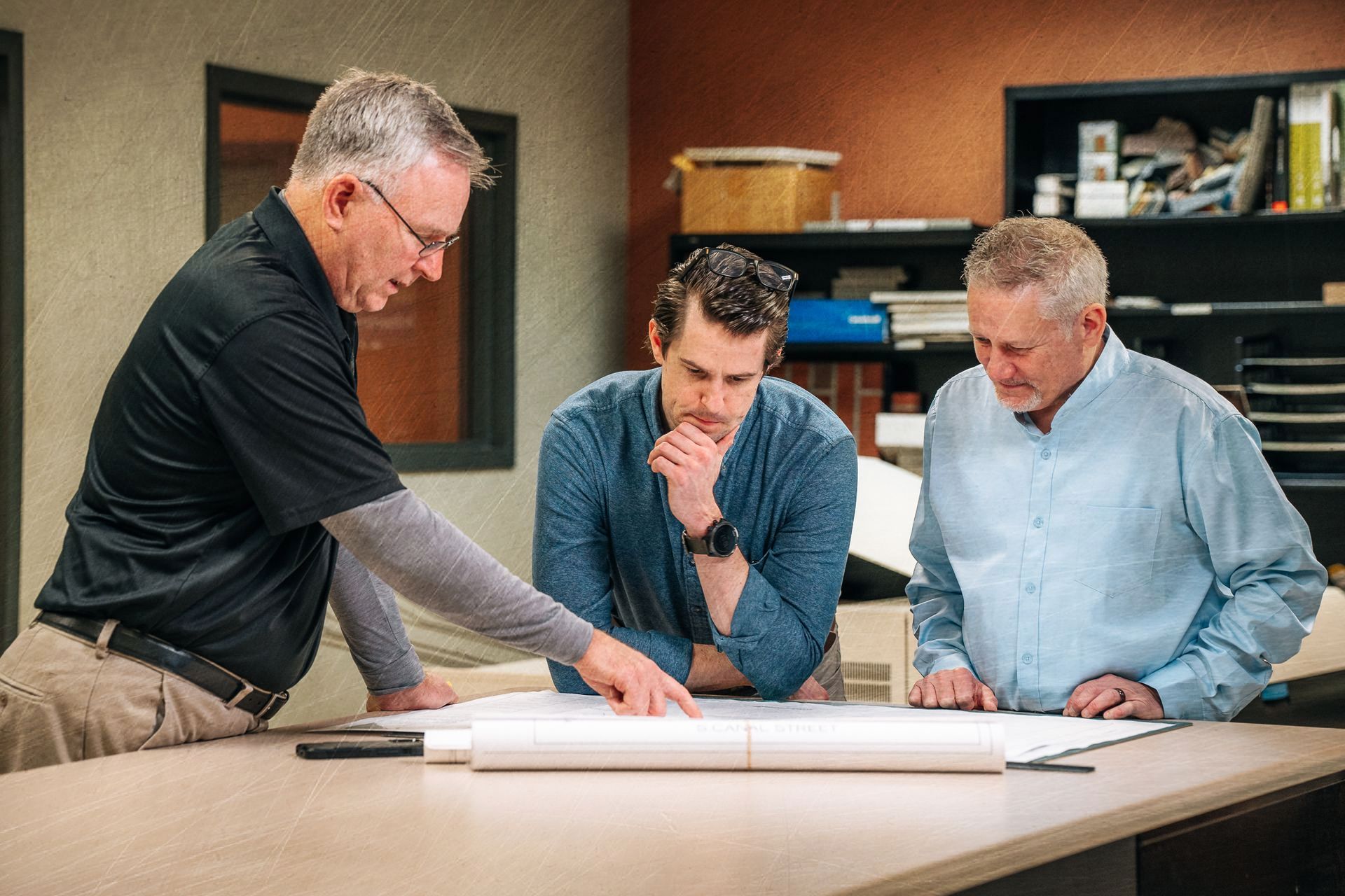 Three men are looking at a blueprint on a table.