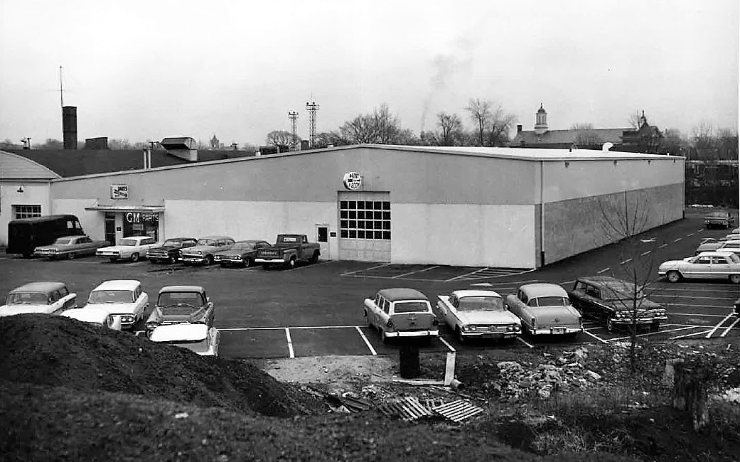 A black and white photo of a building with cars parked in front of it