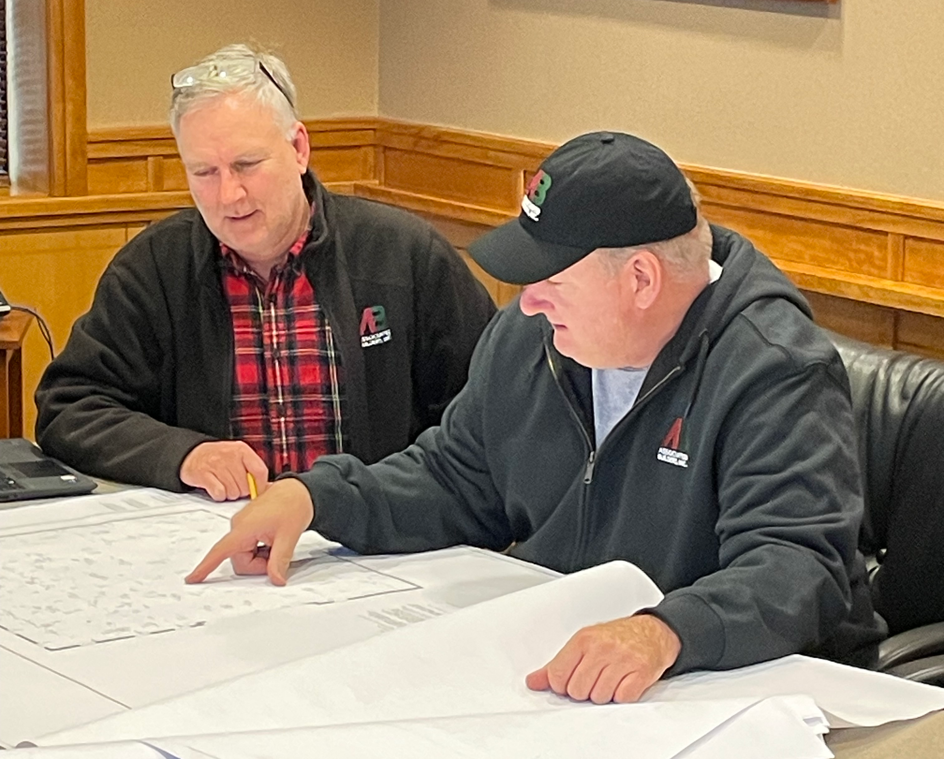 Two men are sitting at a table looking at a blueprint.