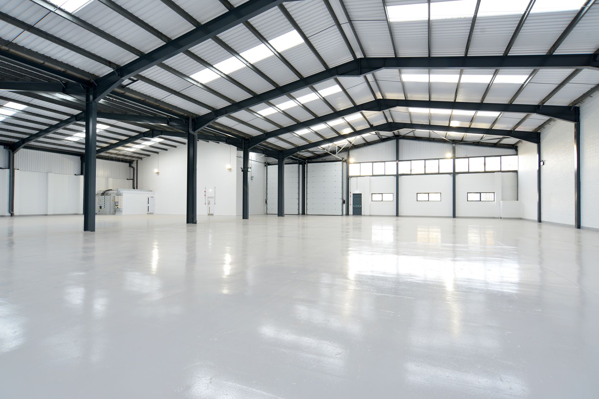 An empty warehouse with a white floor and a metal roof.