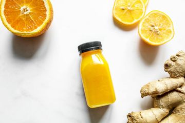 A bottle of orange juice , lemons , and ginger on a table.