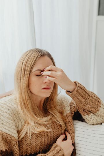 A woman in a sweater is sitting on a couch and rubbing her eyes.