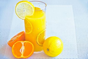 A glass of orange juice with lemon slices and oranges on a table.