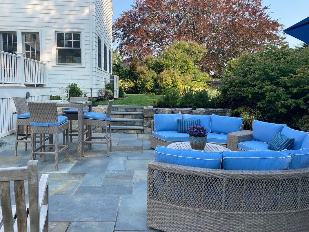 Patio with blue cushioned furniture, stone flooring, and a white house.