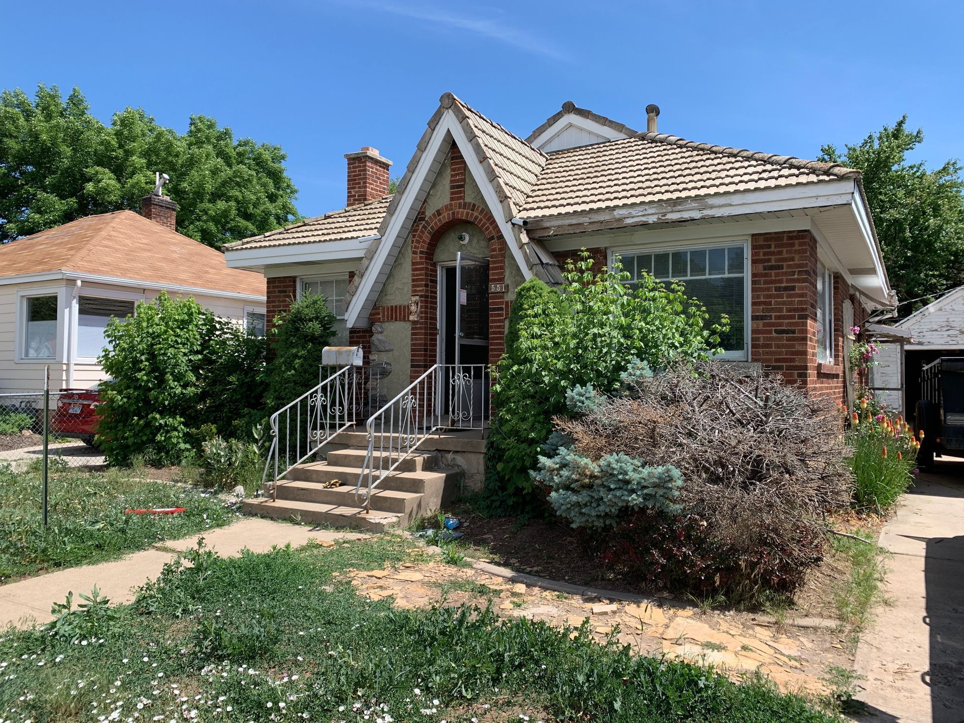 A brick house with a roof that is covered in shingles and a car parked in front of it.