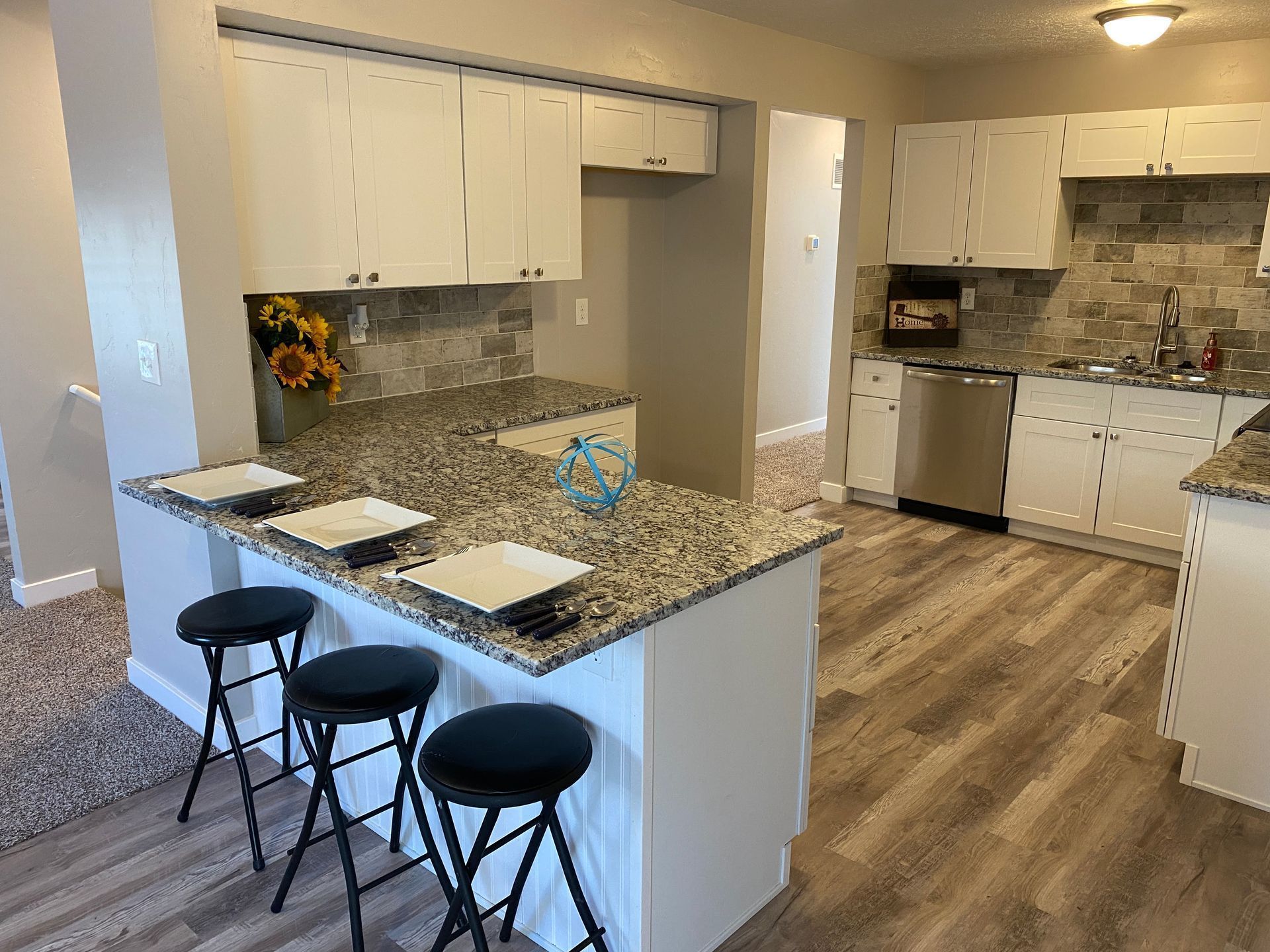 A kitchen with white cabinets , granite counter tops , and stools.