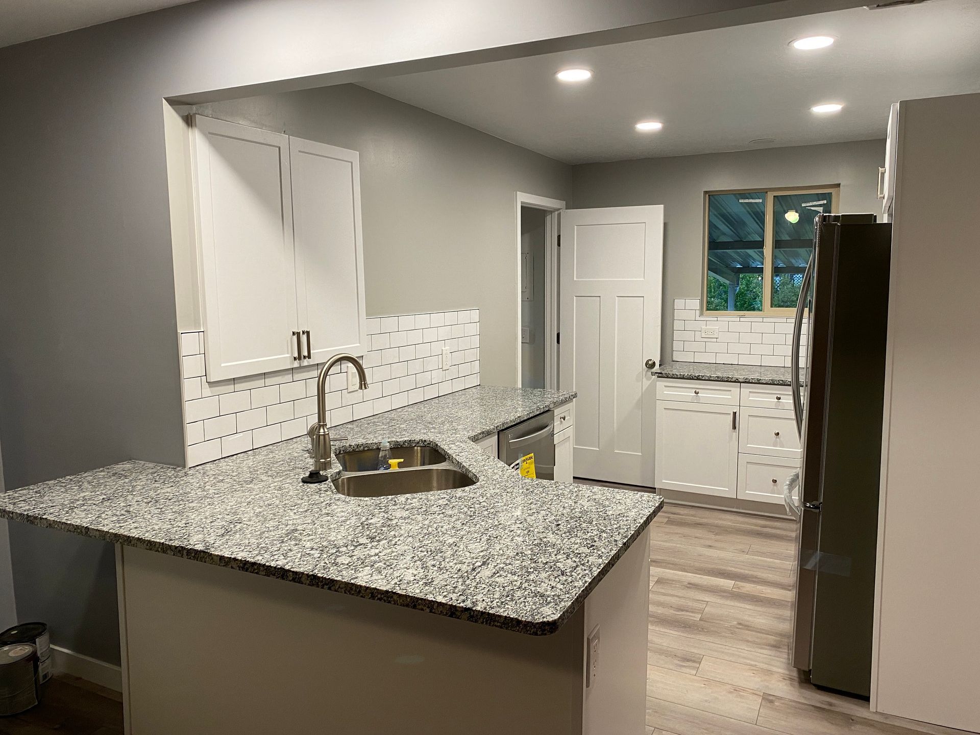 A kitchen with granite counter tops , white cabinets , a sink and a refrigerator.