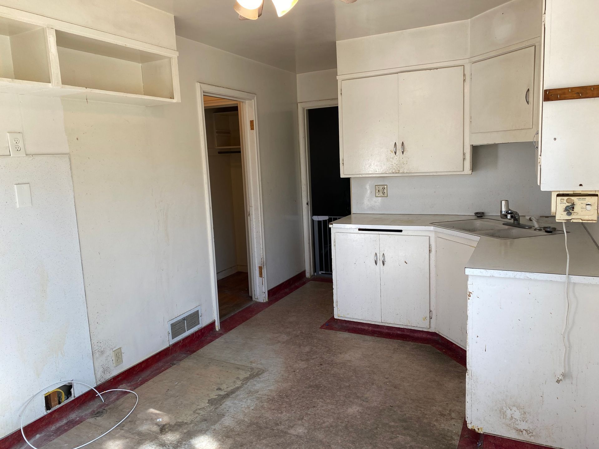 An empty kitchen with white cabinets and red floors.