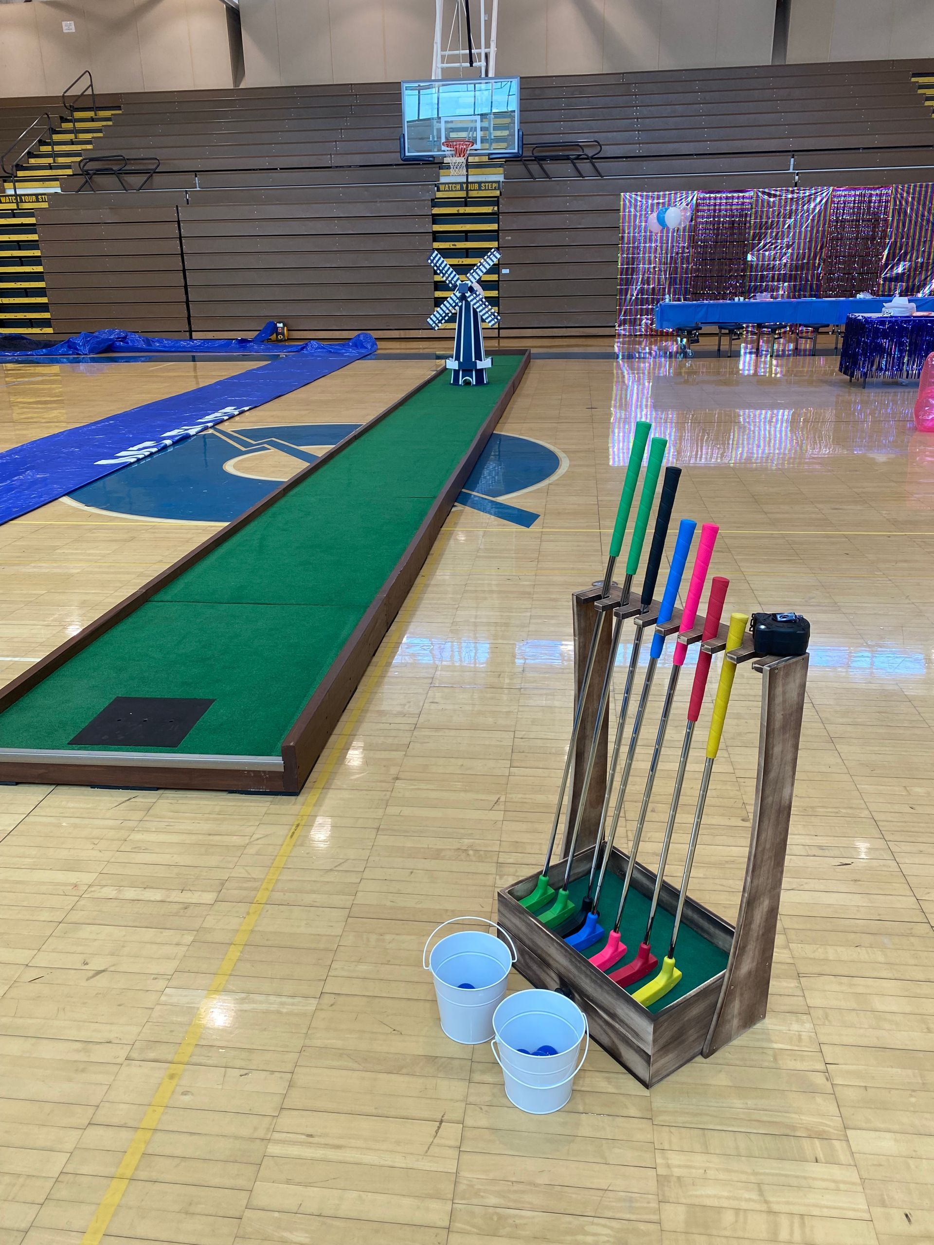 A basketball court with a mini golf course and buckets on the floor.