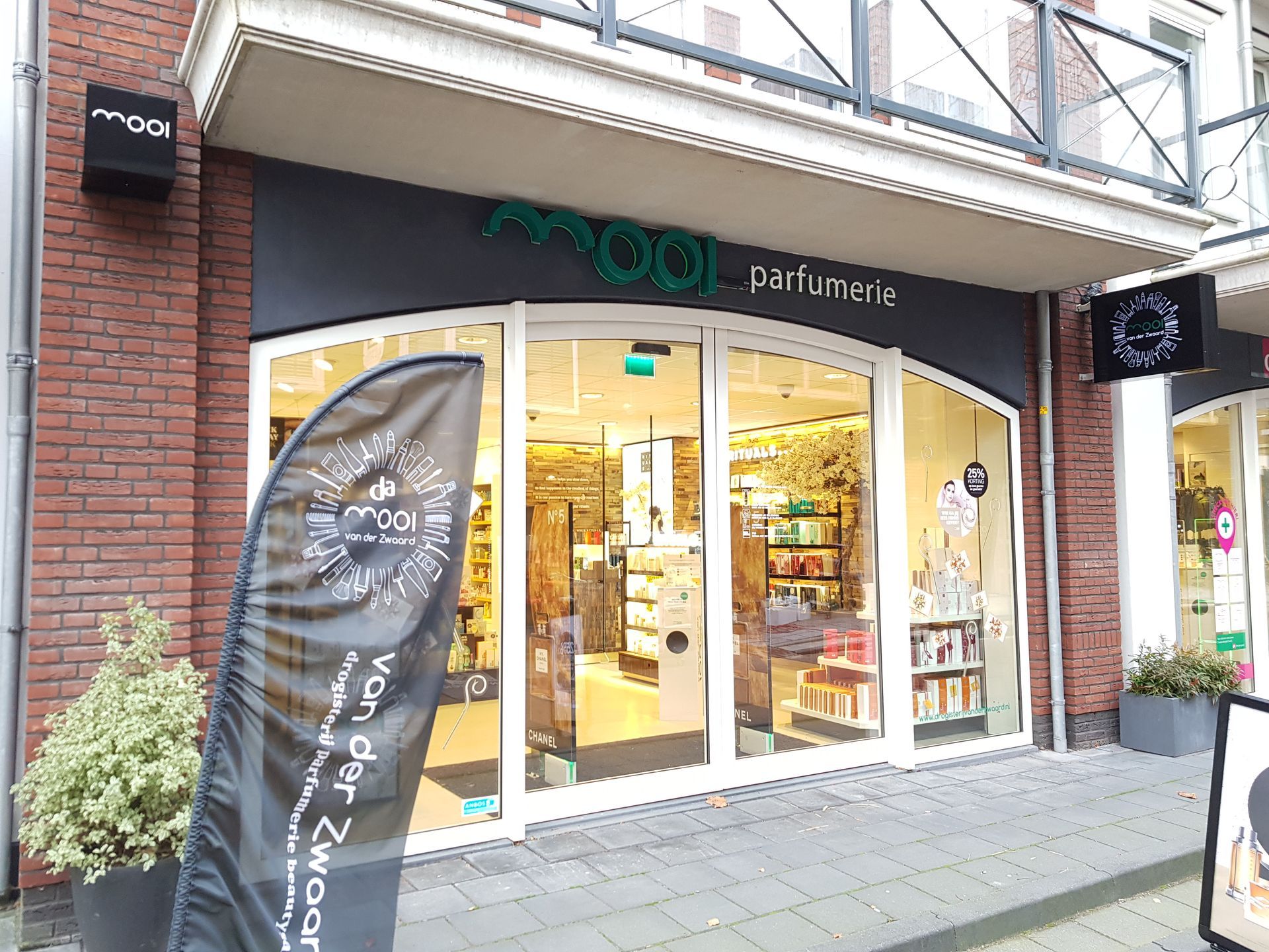 Een winkelpui van parfumerie Moqi met bakstenen muren, een grijs spandoek en een glazen ingang aan de stoep.