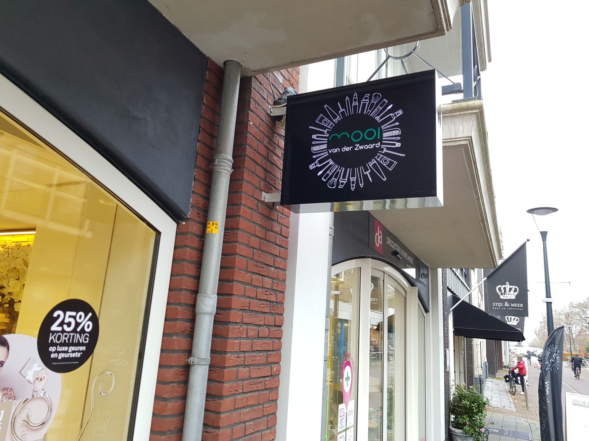 Een winkelpui met een zwart uithangbord waarop een wit, rond logo en de tekst 