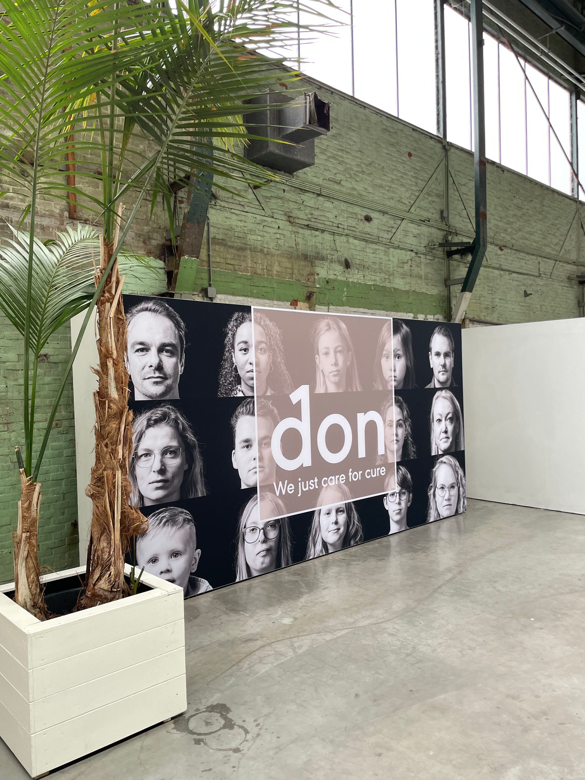 Een raster van zwart-witportretten achter een semi-transparant paneel met de tekst in een rustieke, industriële ruimte.