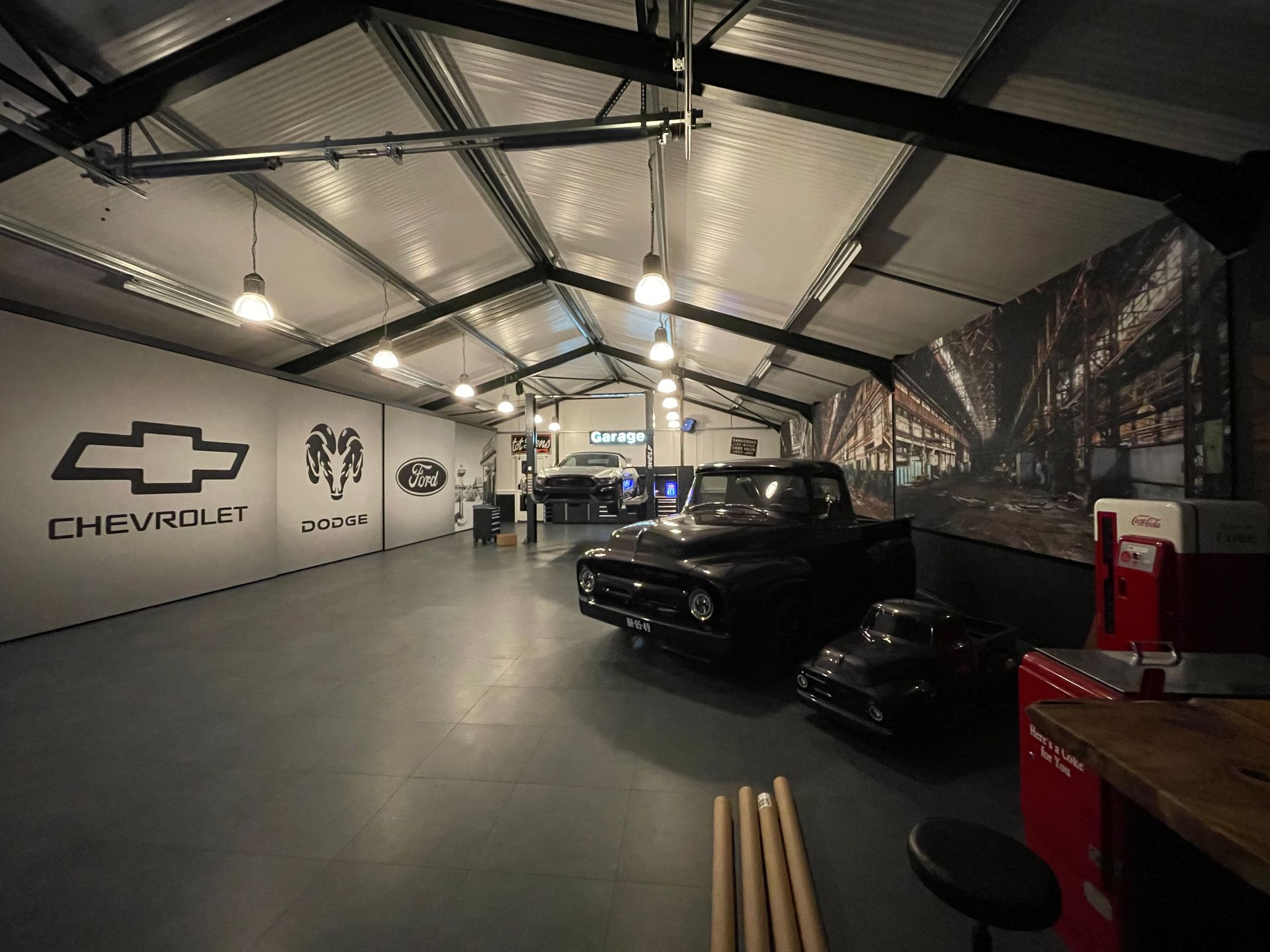 Een ruim garage-interieur met een Chevrolet-logo aan de muur, industriële verlichting en een vintage zwarte vrachtwagen.