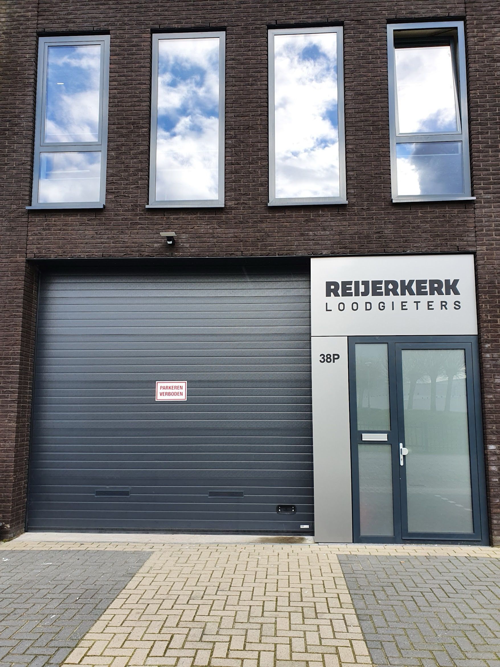 Een gevel met vier ramen bovenaan, een grijze roldeur voor de garage en een ingang met het opschrift