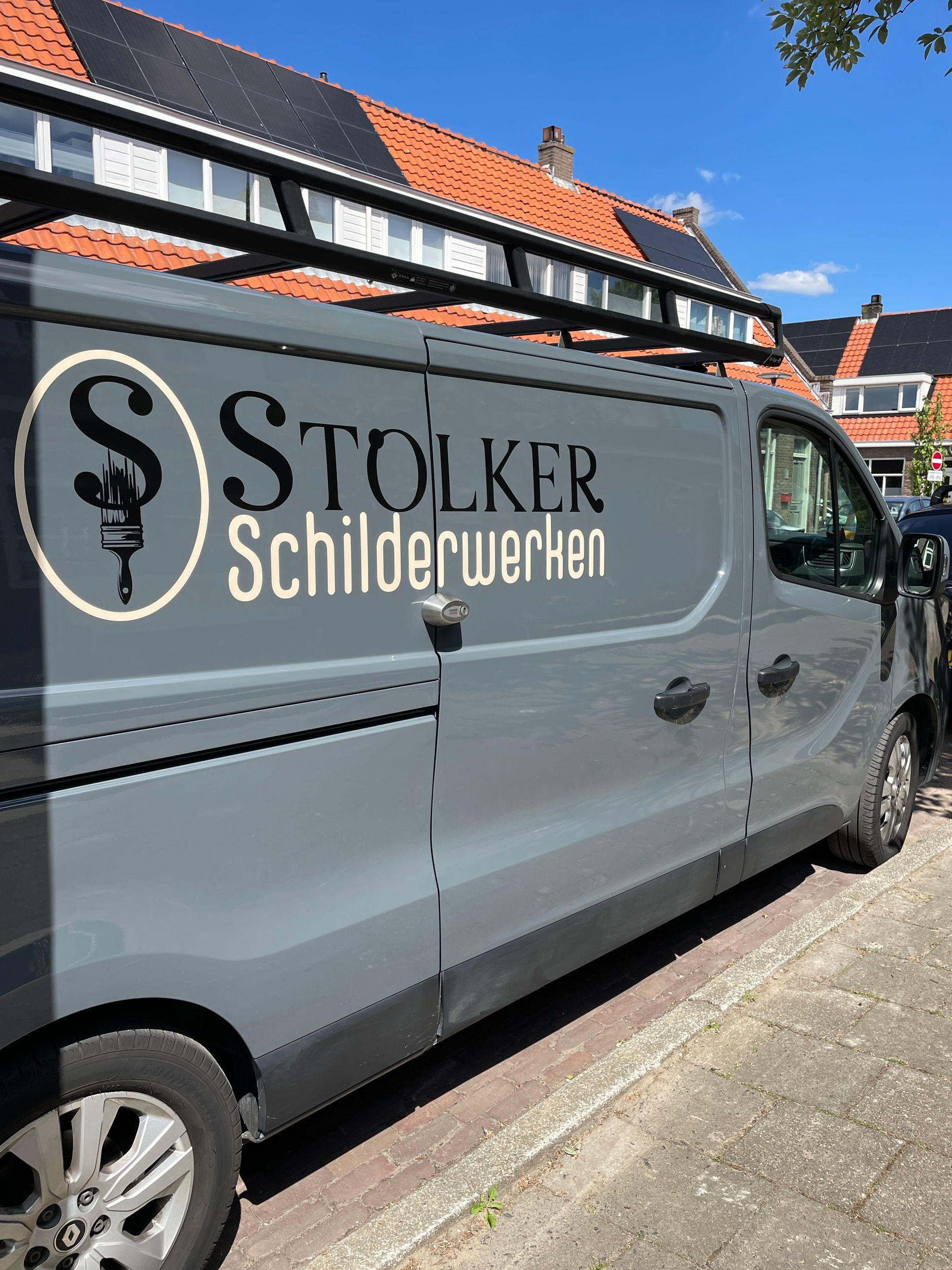 Een grijze werkbus geparkeerd in een straat met het logo van 