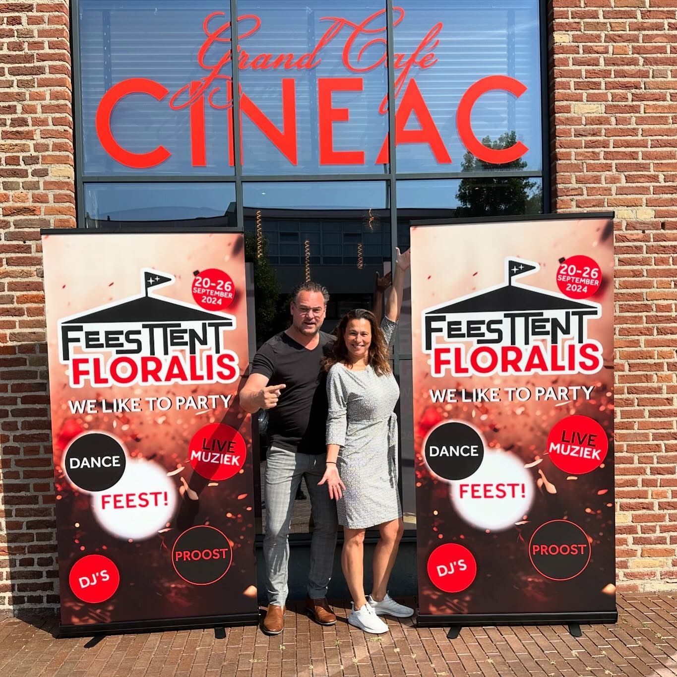 Een man en een vrouw poseren tussen twee reclamebanners voor 