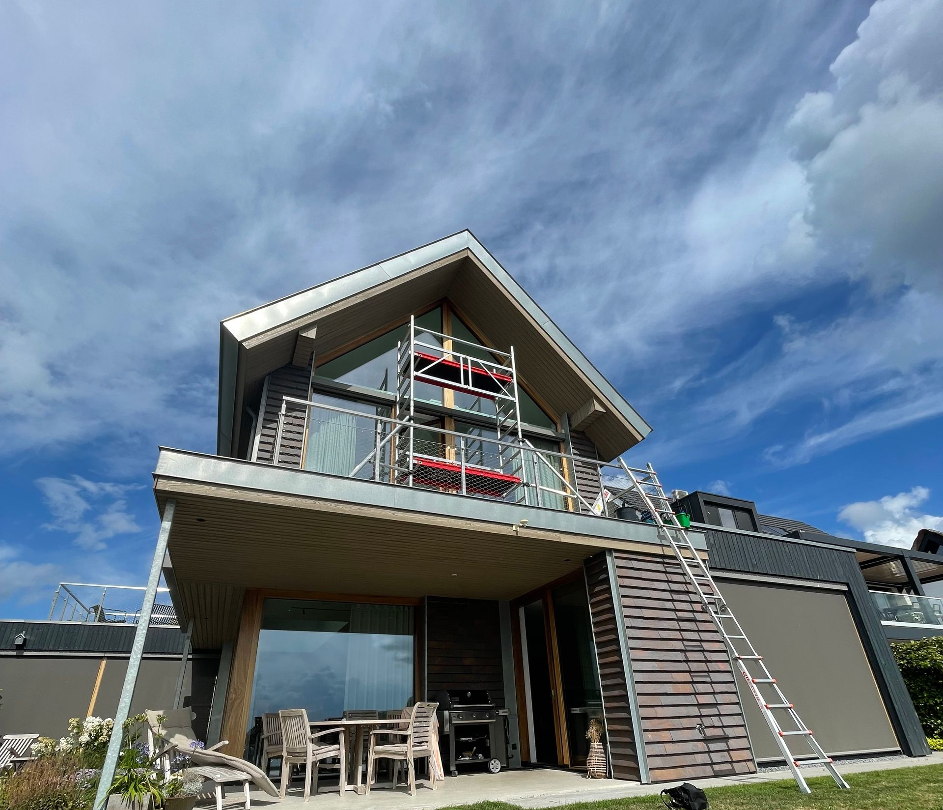 Een modern huis met een houten terrasplafond en balkon in aanbouw, met steigers en een ladder.