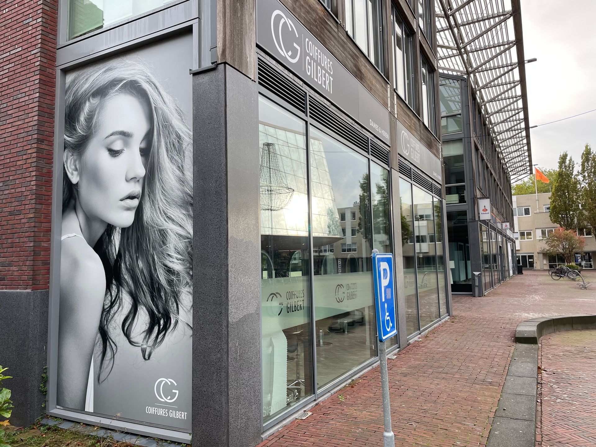 Een etalage met een groot zwart-witportret van een persoon naast de ingang op een bakstenen plein.