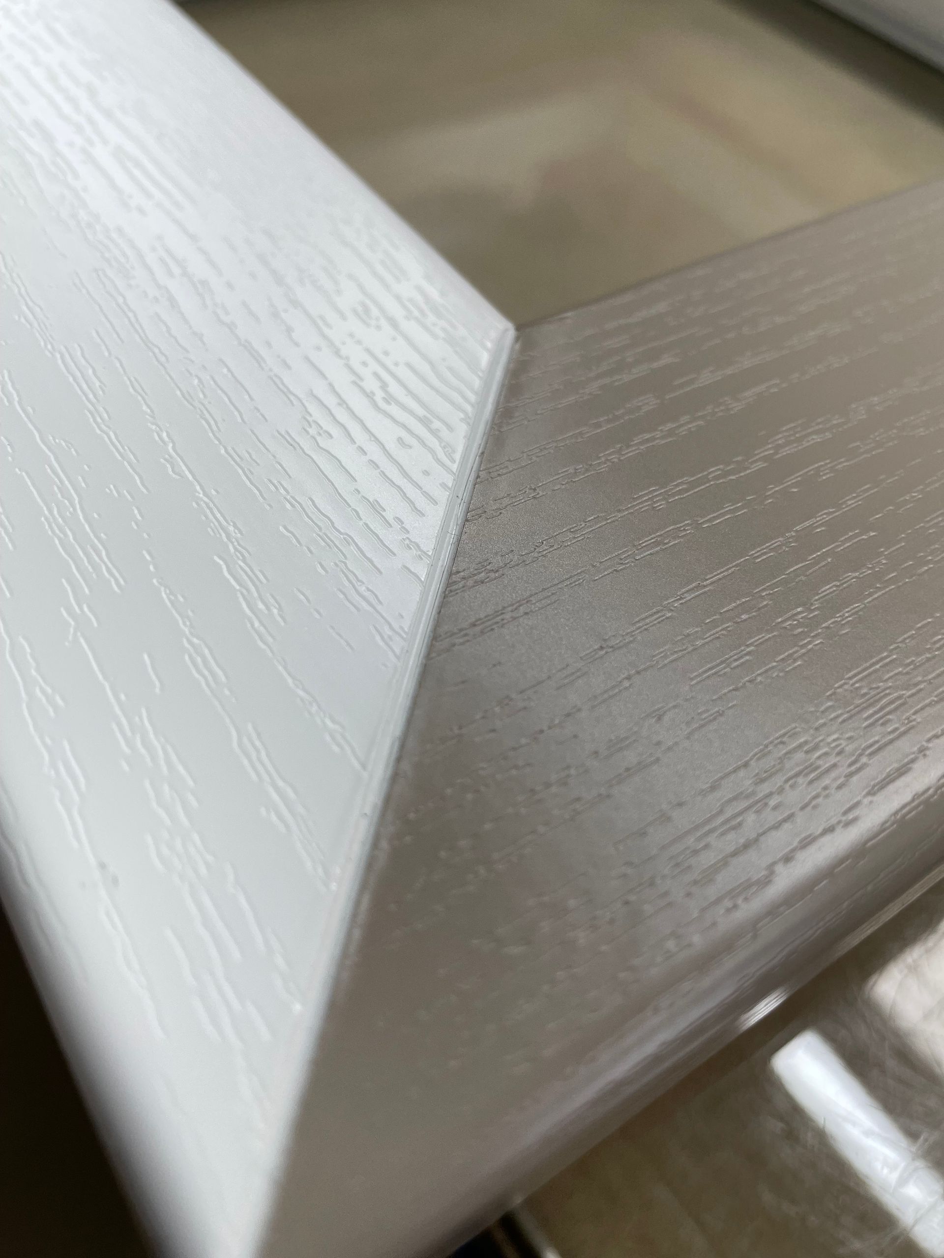 Detailopname van een witte, houtnerfstructuur framehoek met een verstekverbinding.