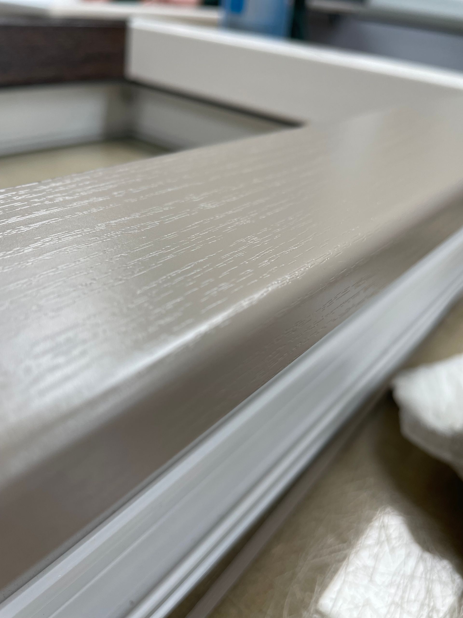 Een close-up, schuin genomen, van een lichtbeige raamkozijn met een subtiele houtnerfstructuur en een witte binnenbekleding.