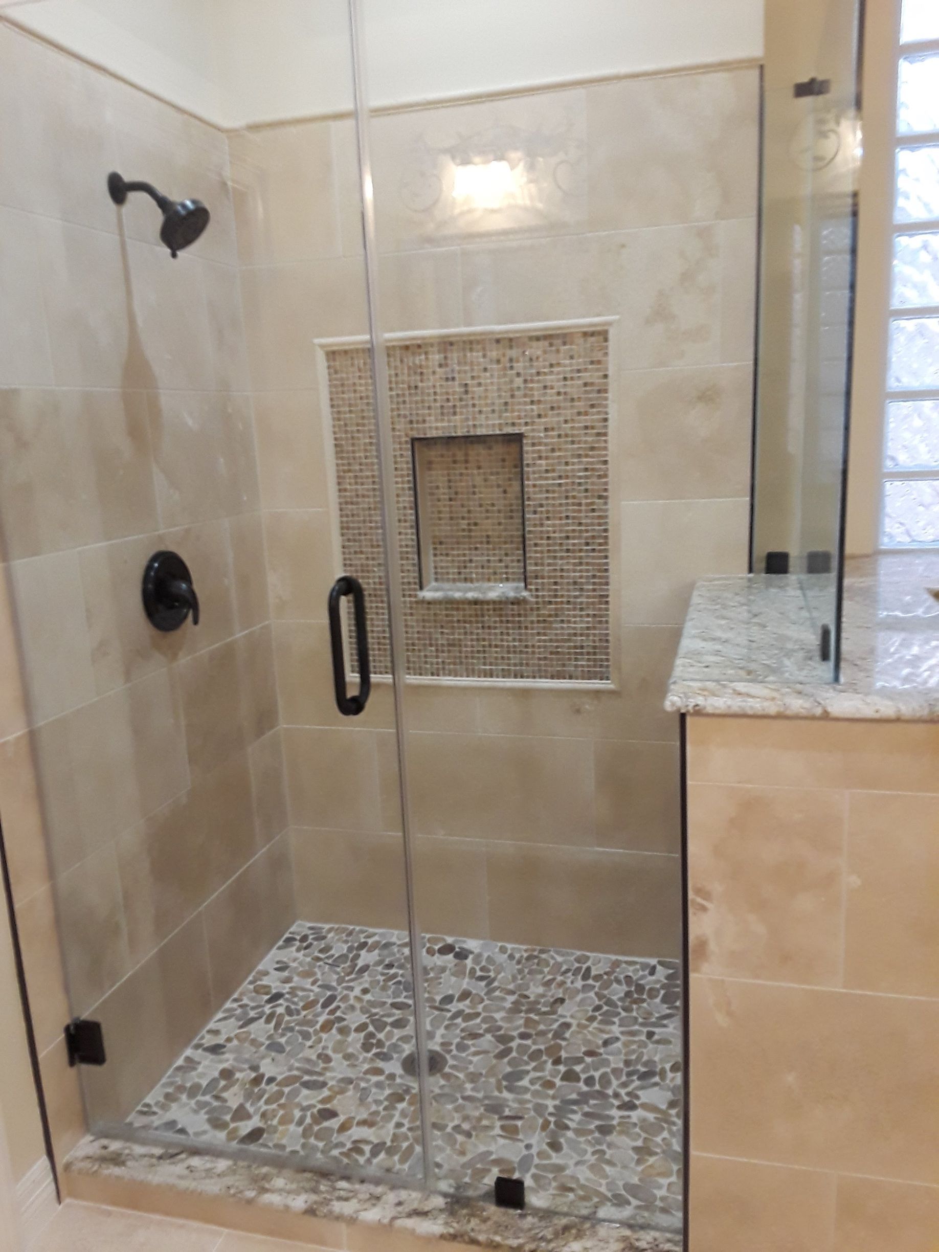 Shower stall with clear glass doors, pebble floor, and stone-tiled walls.